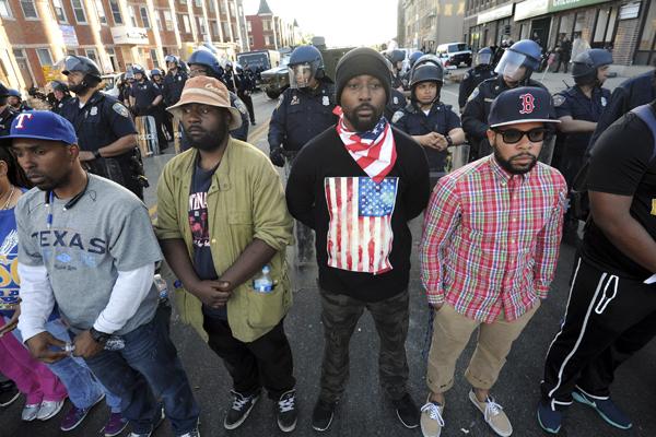 From left, Neil Jennings, 34, from Cherry Hill; Noah Smith, 25, from Pennsylvania  Ave.; Terry Mitchell, 32, from Park Heights, 32; and Ryan Johnson, 28, formerly from Baltimore, stand before a line of officers on April 28, 2015 at North Ave. and Pennsylvania Ave. twenty-four hours after the riots sparked by the death of Freddie Gray in Baltimore, Md. (Algerina Perna/Baltimore Sun/TNS)