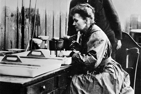 Marie Curie works in a lab alongside a colleague.