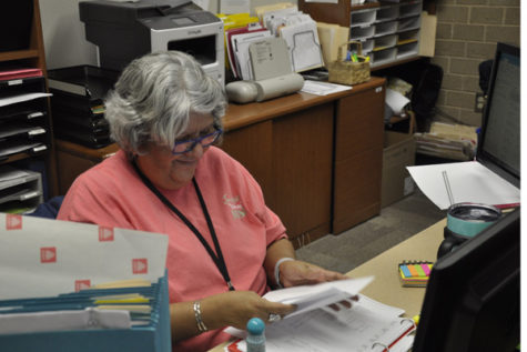 Secretary Lori Carbajal organizes paper in a binder for the counseling office. 