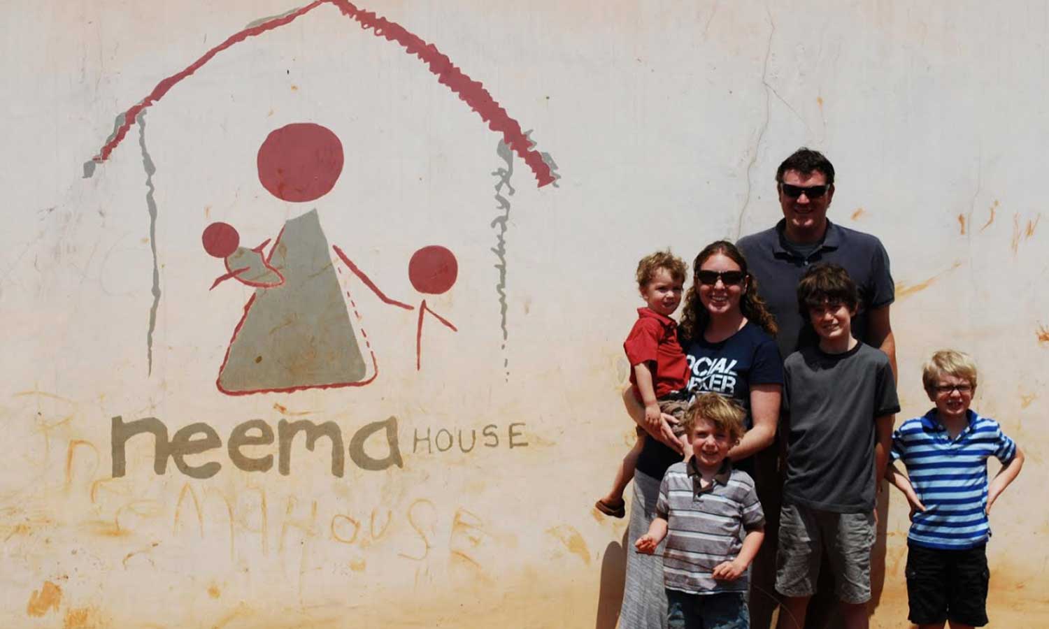 Mr. and Ms. McFaddin stand in front of a Neema House building  with their children. 