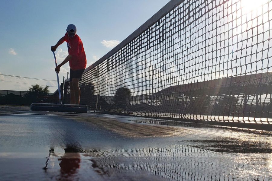 Braydon Martin, 11, squeegees the court after a brief thunderstorm during the varsity tennis game. (Seth Miller photo)