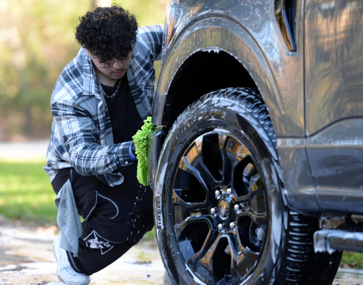 Senior Lazarus Ramos washes the front bumper of a customers car. His mobile detailing business focuses of meeting the customer where they are, prioritizing convenience and comfort.