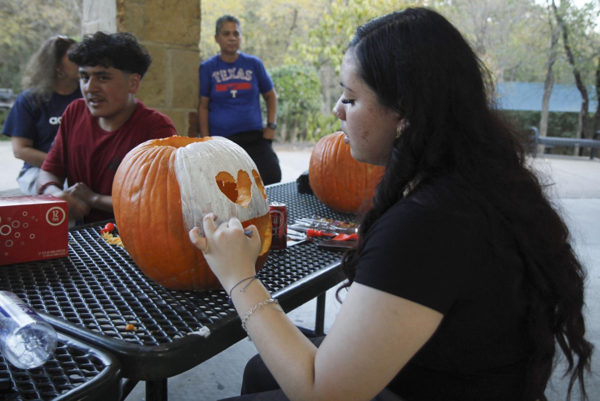 As Halloween music plays in the background, Jazlyn Martinez, 12, sings while painting her pumpkin white.